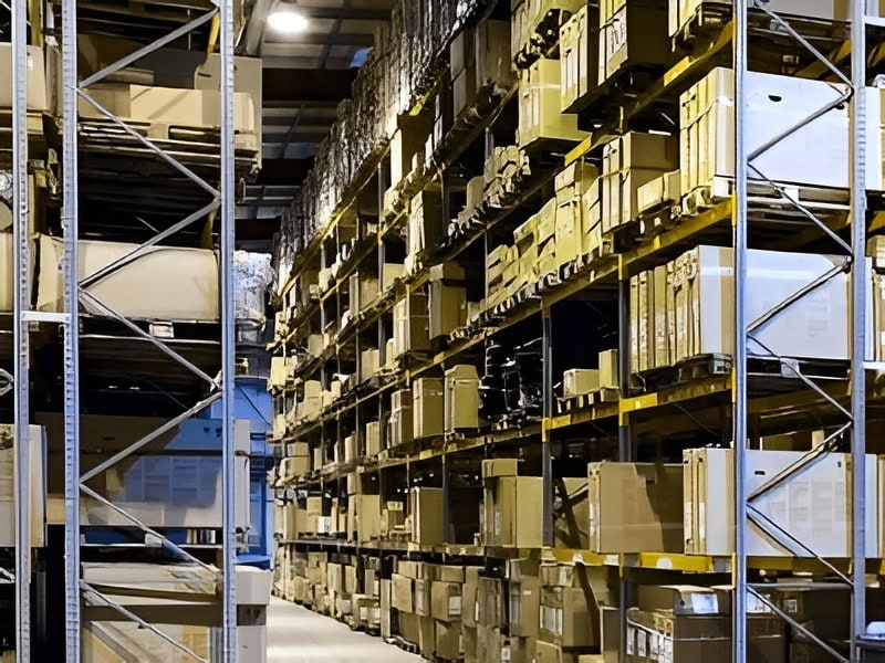 Warehouse aisle with tall metal shelving filled with cardboard boxes and pallets, stretching into the distance.